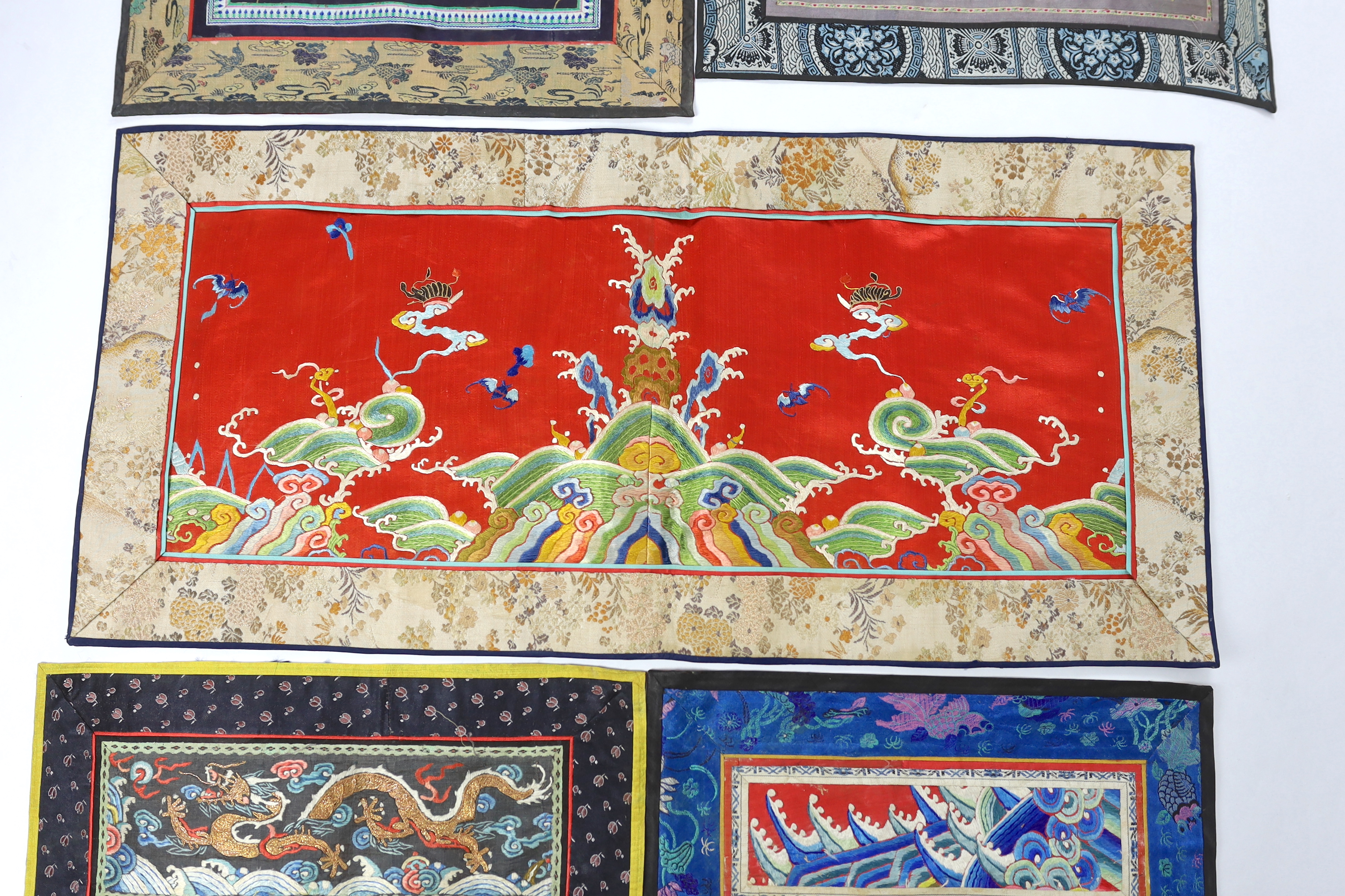 A Chinese late Qing dynasty red silk and polychrome embroidered lishui wave and flaming pearl panel, another smaller metallic dragon panel, an ornate butterfly panel and two other smaller embroidered panels with auspicio